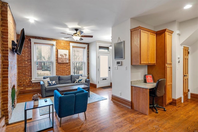 living room with ceiling fan, brick wall, built in desk, and wood-type flooring