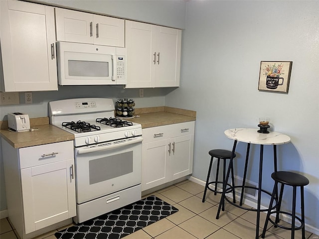 kitchen with light tile patterned floors, white appliances, and white cabinets