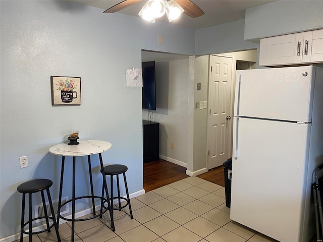 kitchen featuring a breakfast bar area, white cabinetry, light tile patterned floors, white refrigerator, and ceiling fan