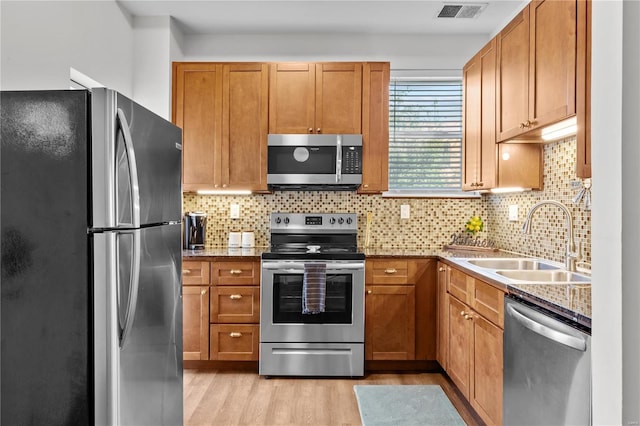 kitchen featuring sink, appliances with stainless steel finishes, backsplash, light stone counters, and light wood-type flooring