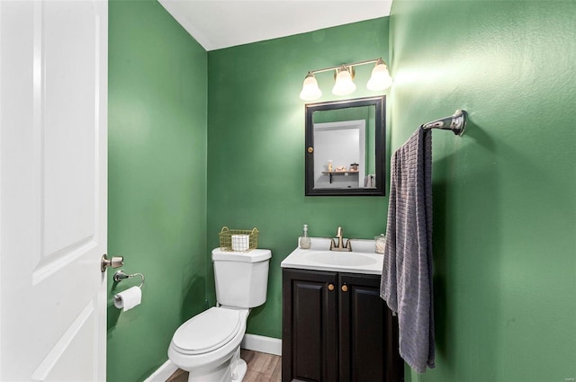 bathroom featuring toilet, baseboards, wood finished floors, and vanity