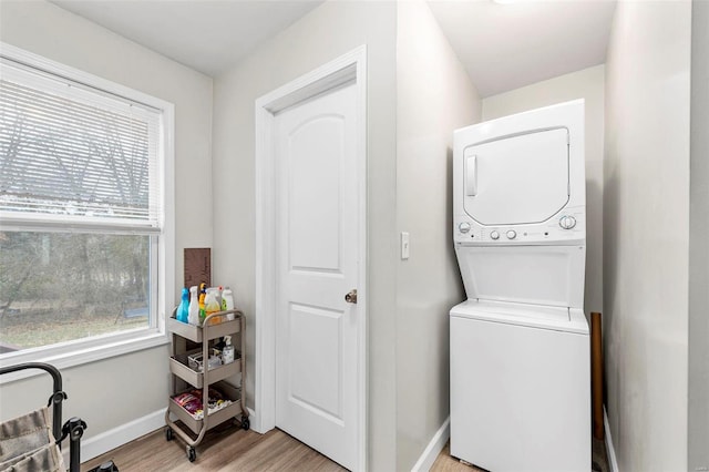 laundry room with stacked washer and dryer, plenty of natural light, baseboards, and light wood-style flooring