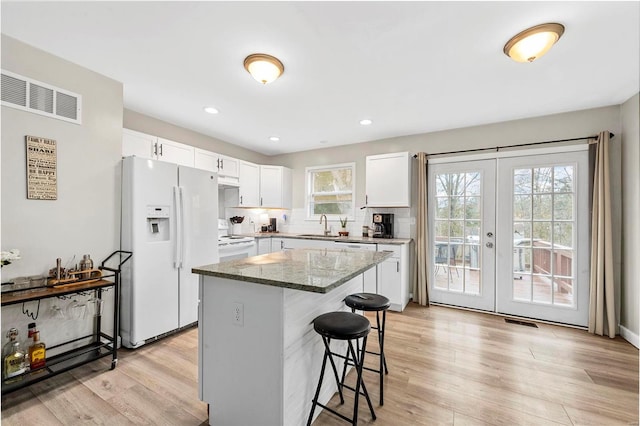 kitchen with a breakfast bar, french doors, visible vents, light wood-style floors, and white fridge with ice dispenser