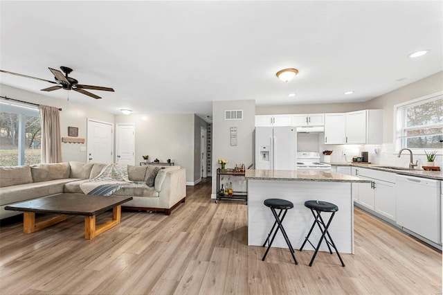 kitchen featuring white appliances, open floor plan, a kitchen breakfast bar, light wood-type flooring, and a sink