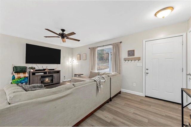 living area featuring a ceiling fan, a glass covered fireplace, baseboards, and wood finished floors