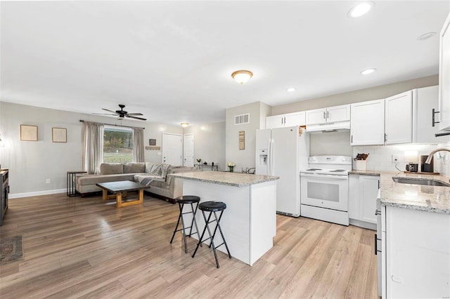 kitchen featuring under cabinet range hood, white appliances, a sink, light wood-style floors, and a kitchen bar