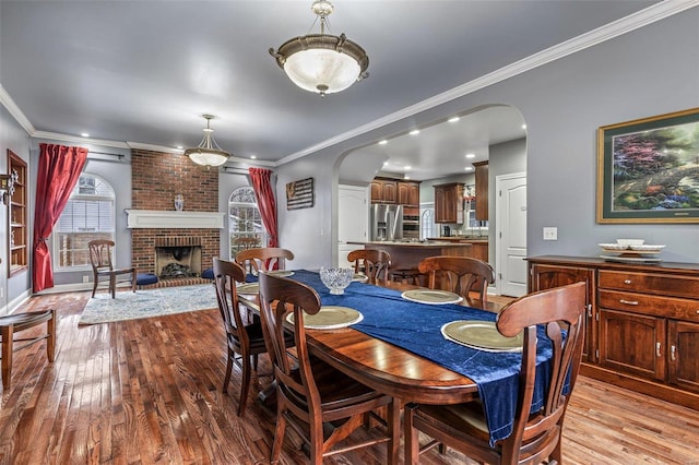 dining room featuring crown molding, a brick fireplace, and light wood-type flooring