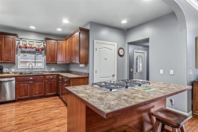 kitchen with sink, a kitchen breakfast bar, stainless steel appliances, light stone countertops, and light hardwood / wood-style floors