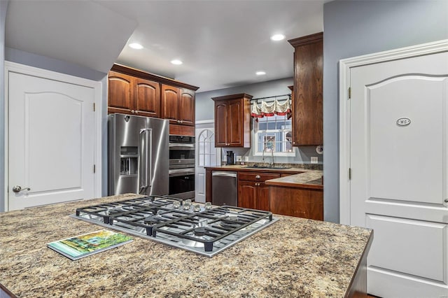 kitchen with stainless steel appliances, a center island, light stone countertops, and sink