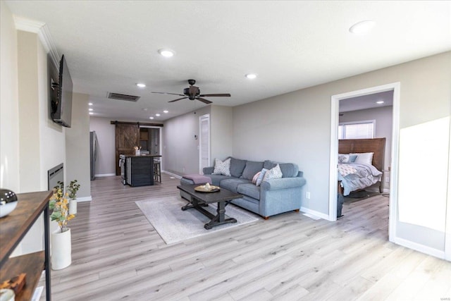 living room with ceiling fan, a barn door, and light hardwood / wood-style floors