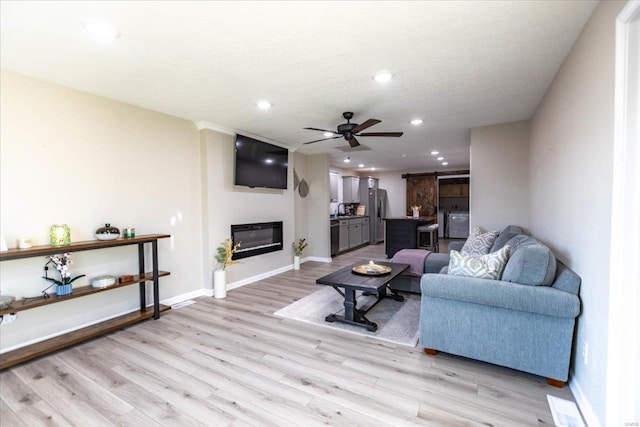 living room featuring ceiling fan, sink, a textured ceiling, and light wood-type flooring