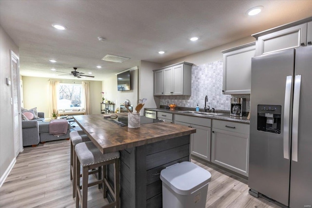 kitchen featuring stainless steel refrigerator with ice dispenser, butcher block counters, sink, gray cabinetry, and tasteful backsplash