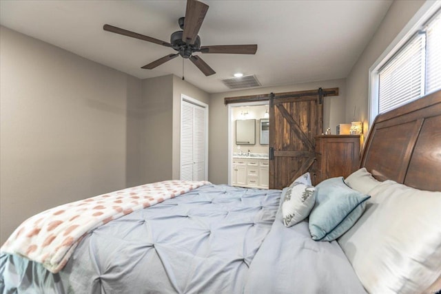 bedroom with ensuite bathroom, sink, a closet, ceiling fan, and a barn door