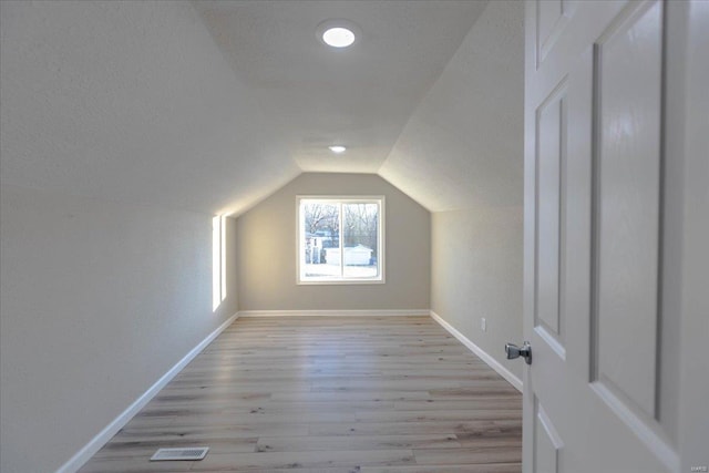 additional living space with light hardwood / wood-style floors, vaulted ceiling, and a textured ceiling