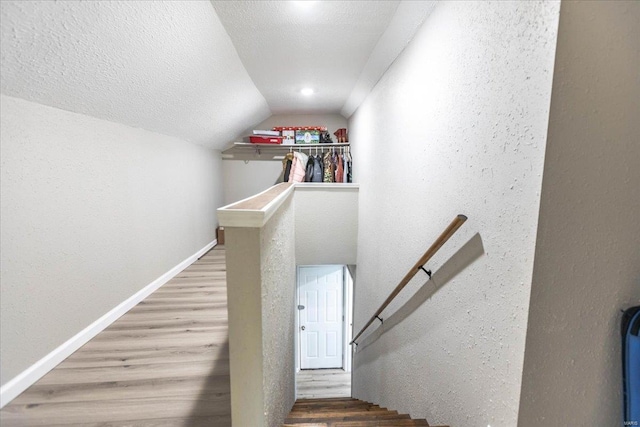 staircase with lofted ceiling, wood-type flooring, and a textured ceiling