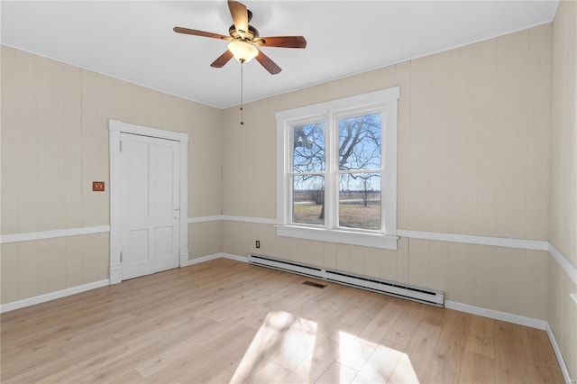 empty room featuring ceiling fan, light wood-type flooring, and baseboard heating