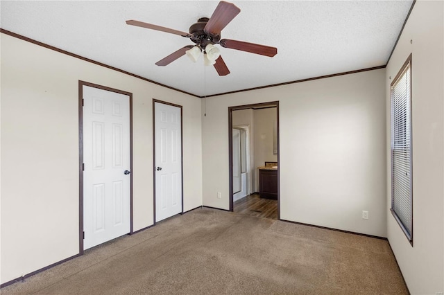 unfurnished bedroom featuring connected bathroom, light carpet, a textured ceiling, multiple closets, and ornamental molding