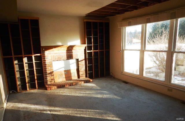 unfurnished living room featuring a brick fireplace, carpet floors, and a healthy amount of sunlight