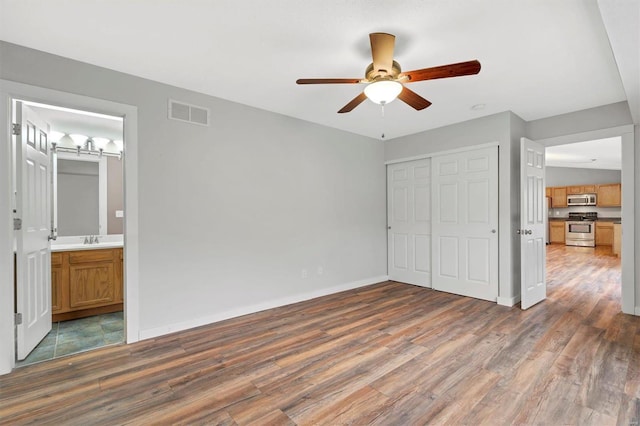 unfurnished bedroom with a barn door, sink, dark hardwood / wood-style flooring, and a closet