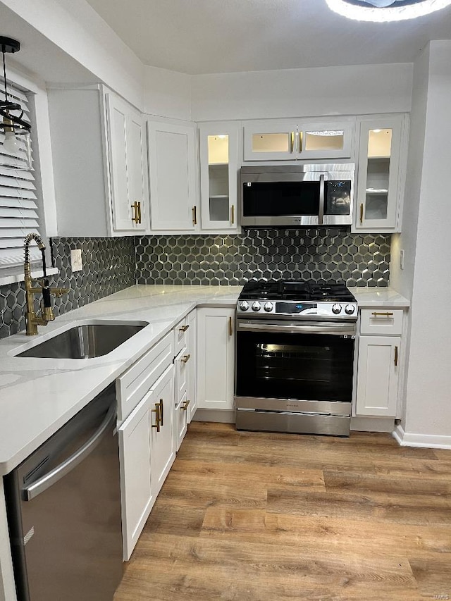 kitchen featuring appliances with stainless steel finishes, white cabinetry, sink, light stone countertops, and light hardwood / wood-style flooring