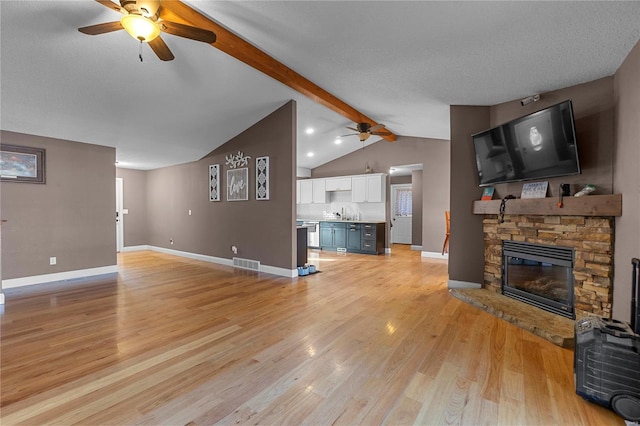 living room with a fireplace, lofted ceiling with beams, light wood-type flooring, ceiling fan, and a textured ceiling