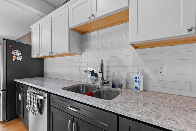 kitchen with sink, white cabinetry, stainless steel appliances, light stone countertops, and a textured ceiling