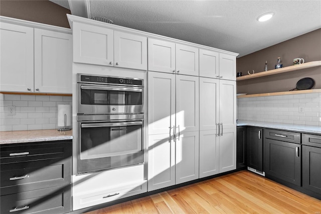 kitchen featuring white cabinetry, light wood-type flooring, double oven, and decorative backsplash