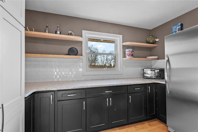 kitchen with light hardwood / wood-style flooring, stainless steel fridge, light stone countertops, a textured ceiling, and decorative backsplash