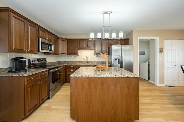 kitchen with pendant lighting, sink, light hardwood / wood-style flooring, appliances with stainless steel finishes, and a center island