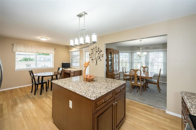 kitchen featuring light stone counters, decorative light fixtures, a center island, a chandelier, and light hardwood / wood-style flooring