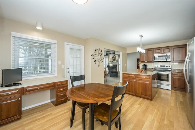 kitchen featuring light stone counters, light hardwood / wood-style flooring, appliances with stainless steel finishes, pendant lighting, and decorative backsplash