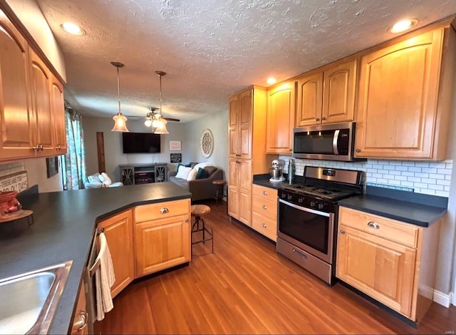 kitchen with dark wood-type flooring, stainless steel appliances, kitchen peninsula, and hanging light fixtures