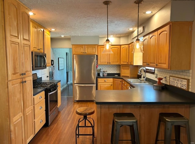 kitchen with dark wood-type flooring, a kitchen bar, sink, appliances with stainless steel finishes, and pendant lighting