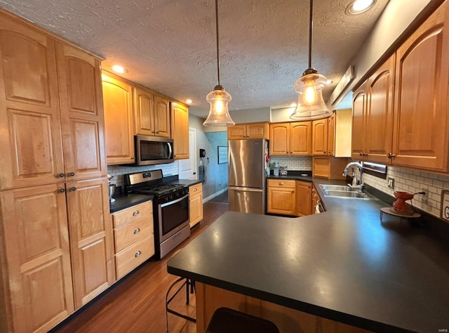 kitchen with pendant lighting, sink, a breakfast bar, appliances with stainless steel finishes, and dark hardwood / wood-style floors