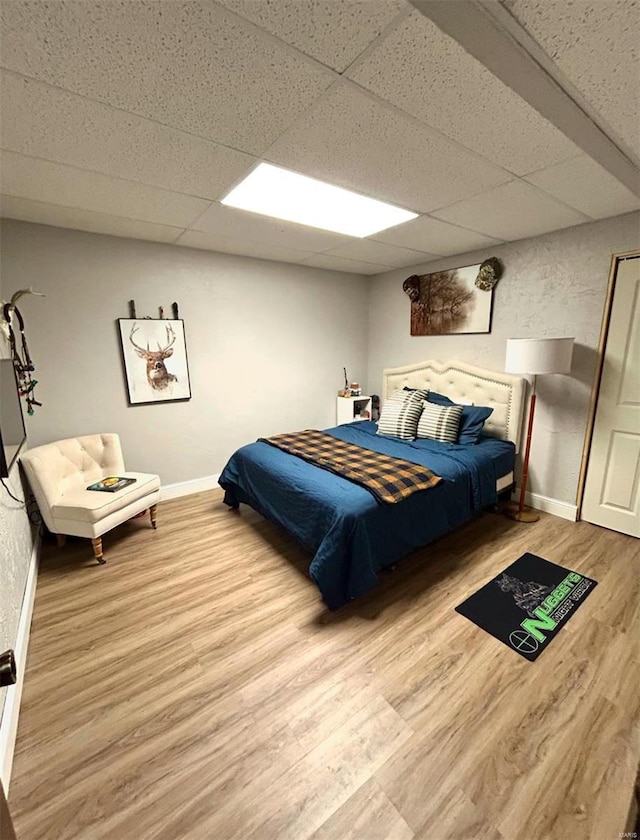 bedroom with a drop ceiling and light wood-type flooring