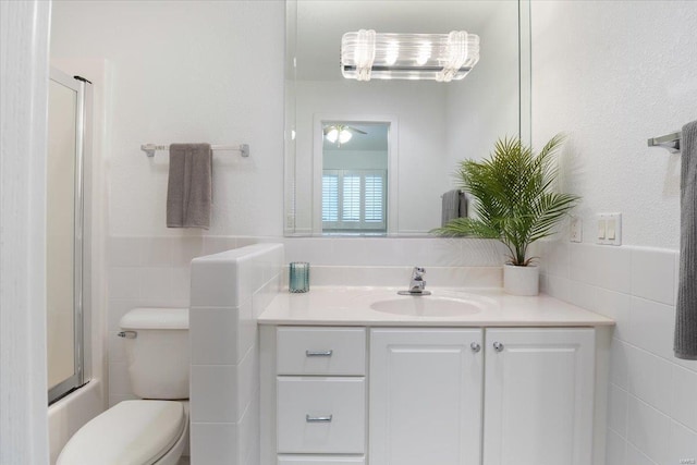 full bathroom with shower / bath combination with glass door, vanity, toilet, and tile walls