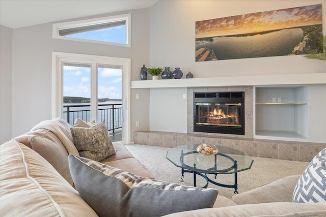 living room with light carpet, a water view, a tiled fireplace, built in shelves, and vaulted ceiling