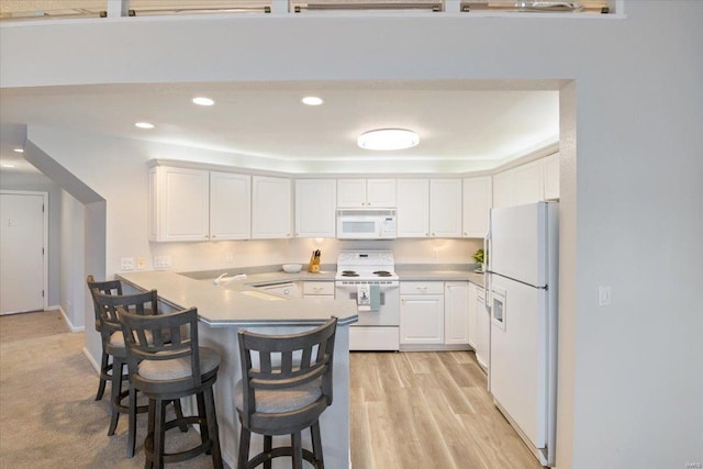 kitchen with white appliances, kitchen peninsula, a breakfast bar, and white cabinets