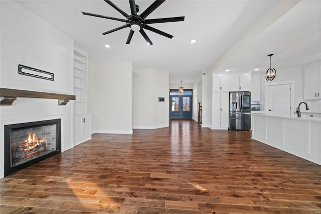 unfurnished living room featuring built in shelves, dark wood-type flooring, a large fireplace, and ceiling fan with notable chandelier