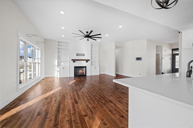 unfurnished living room featuring dark wood-type flooring, ceiling fan, and built in shelves