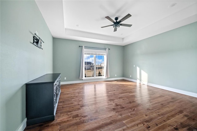 unfurnished living room with a tray ceiling, dark hardwood / wood-style floors, and ceiling fan