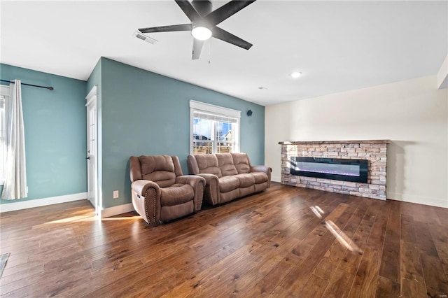 living room with hardwood / wood-style flooring, a stone fireplace, and ceiling fan