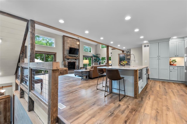 kitchen featuring a center island with sink, a stone fireplace, a breakfast bar area, and light hardwood / wood-style flooring