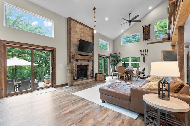 living room with ceiling fan, high vaulted ceiling, light wood-type flooring, and a fireplace