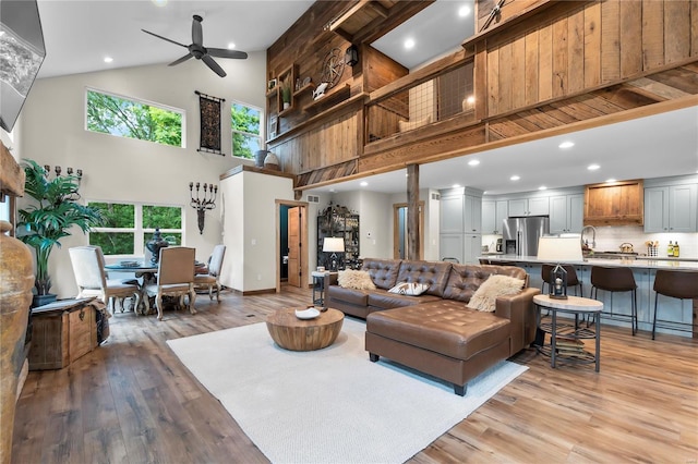 living room with high vaulted ceiling, light hardwood / wood-style floors, sink, and ceiling fan