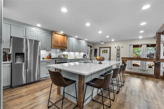 kitchen with stainless steel fridge, a breakfast bar area, a kitchen island with sink, gray cabinetry, and light stone countertops