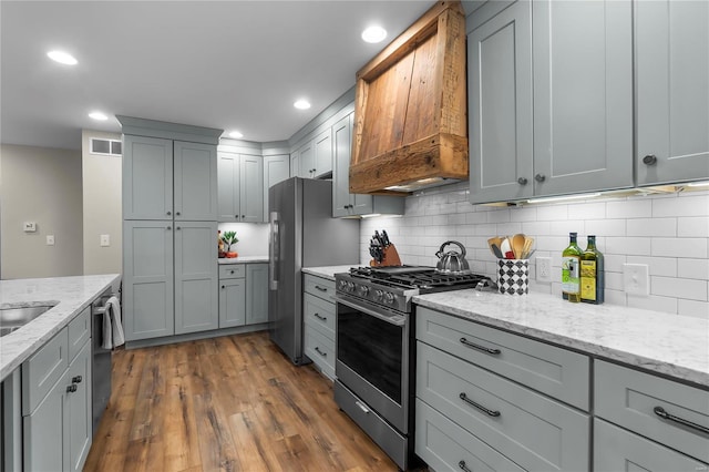 kitchen with gray cabinets, light stone countertops, custom range hood, and appliances with stainless steel finishes