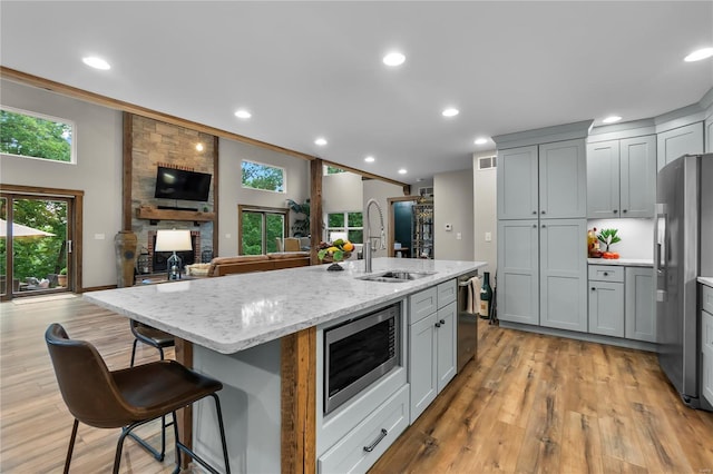 kitchen with a kitchen island with sink, light stone countertops, stainless steel appliances, and gray cabinetry