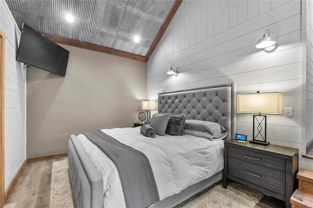 bedroom with lofted ceiling, wooden walls, and light wood-type flooring