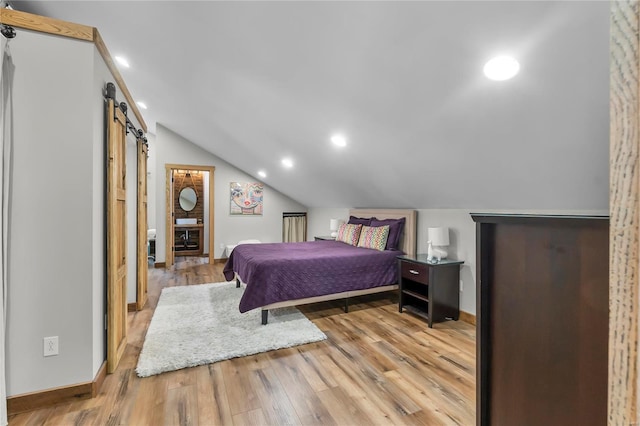 bedroom with a barn door, vaulted ceiling, and light wood-type flooring